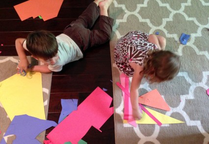 Laine arranging shapes to make a boat; Blaise cutting.